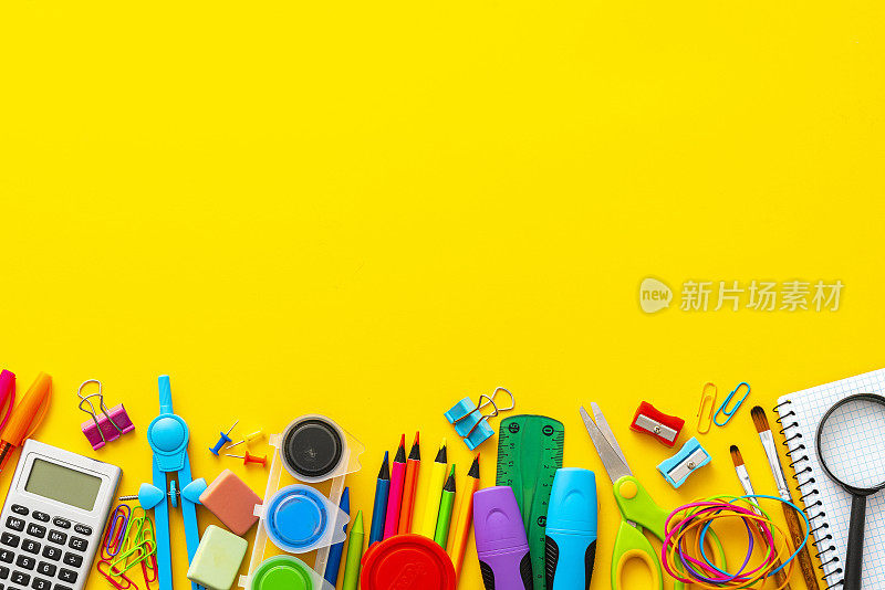 一大群五颜六色的学习用品排列在黄色背景的底部。副本的空间。