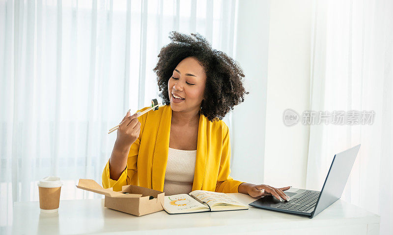 年轻的非洲女性在办公室午餐休息时享用中餐的肖像，女员工拿着筷子在家庭办公室的工作场所吃外卖日本或韩国寿司盒饭。