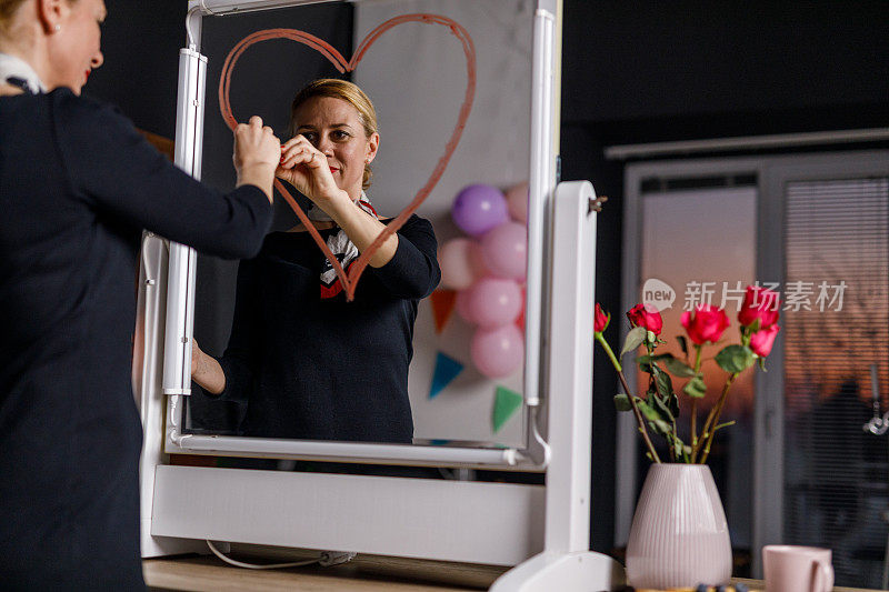 一个快乐的女人站在镜子前，用红色的口红画着一颗心
