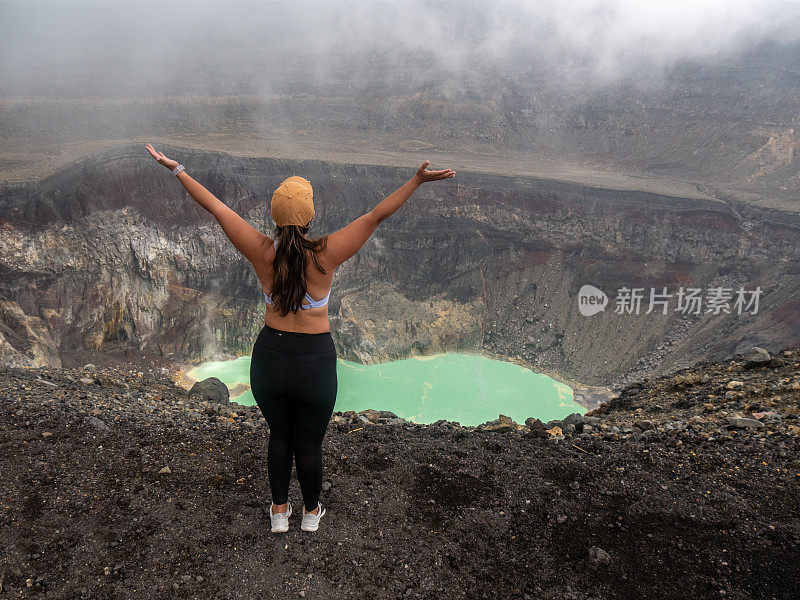 快乐的女人凝视着火山口，她伸开双臂站着