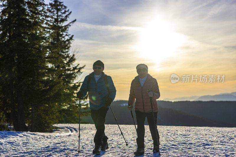 老夫妇拄着登山杖在雪景上行走