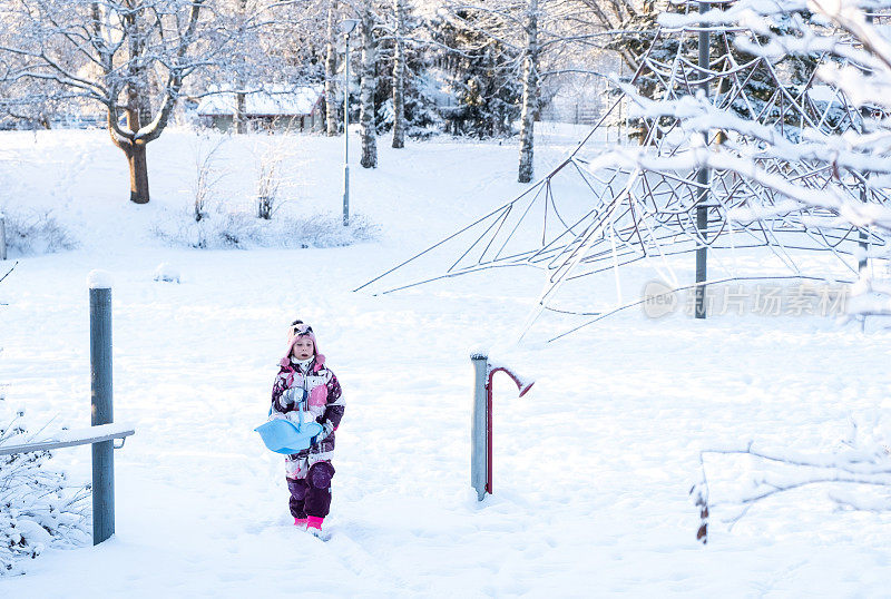 一个白人女孩，一个8岁的孩子，走在操场上，手里拿着一个洋娃娃。冬日公园里的儿童游乐场。