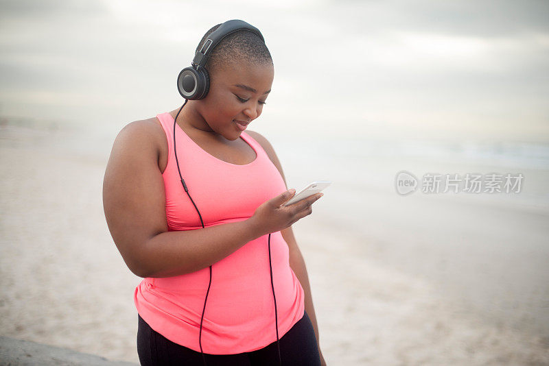 手机、音乐和大码黑人女性在沙滩上进行健康、健身或有氧运动。训练，锻炼或运动，快乐的年轻跑步者戴着耳机，播放流媒体锻炼播放列表或音频