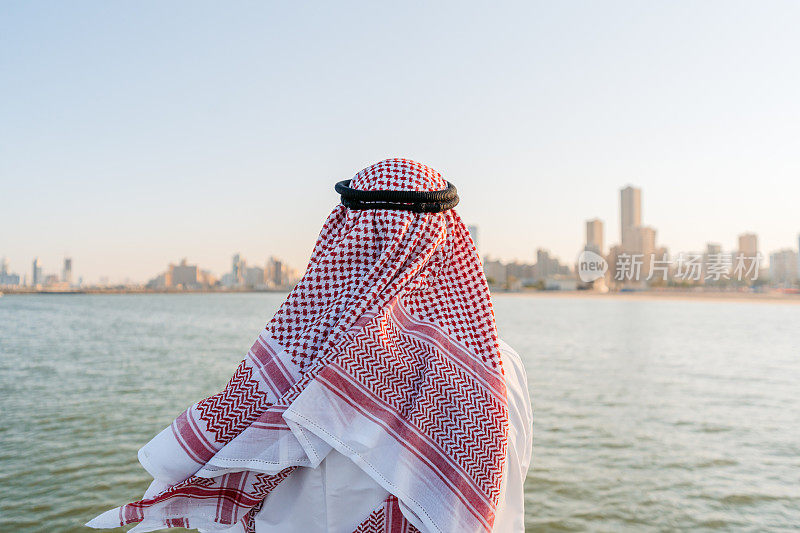 身穿头巾和头巾的年轻男子在科威特市的海滩上欣赏风景