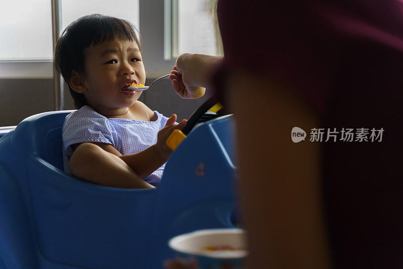 亚洲患病的小男孩在病毒病康复期间坐在医院的玩具车上，母亲在病房喂饭。可爱的亚洲孩子感染病毒住院了。婴儿保健医疗理念。