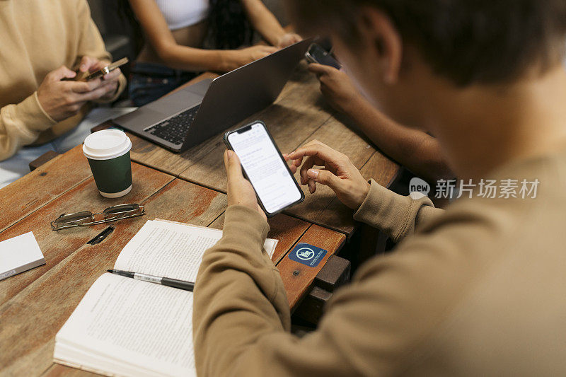 年轻学生和朋友坐在咖啡桌旁玩手机