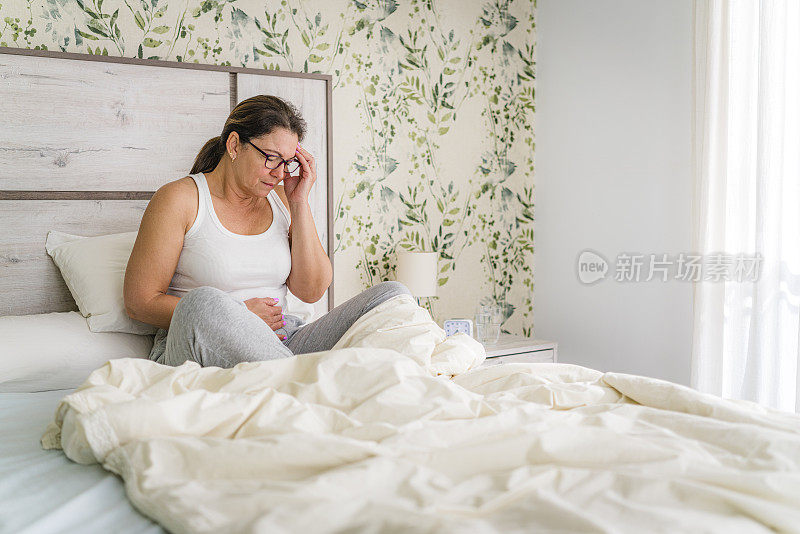 女人坐在床上抚摸着她疼痛的头和肚子