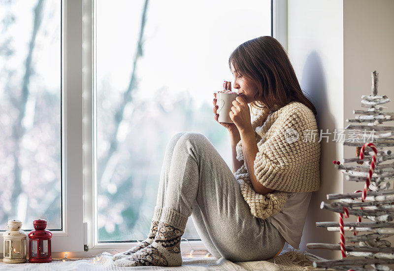 年轻漂亮的女人坐在窗台上喝着热咖啡