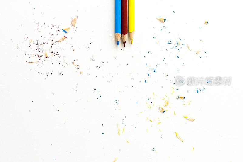 三支彩色铅笔，白色铅笔上散落着刨花
