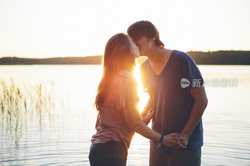 初恋:一对年轻的情侣在夕阳下亲吻，背景是湖水