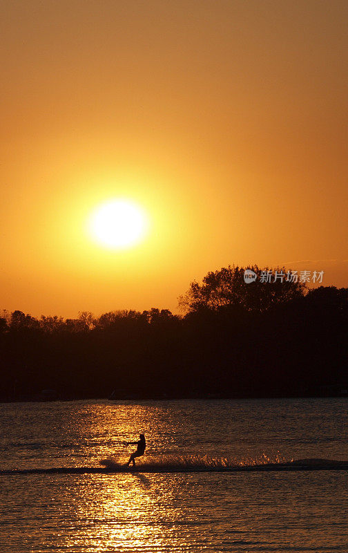 激流滑水者的剪影映衬在金色的湖水和夕阳的映衬下。