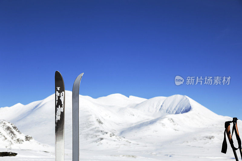 滑雪板和滑雪杆在多山的冬季景观与蓝色的天空。