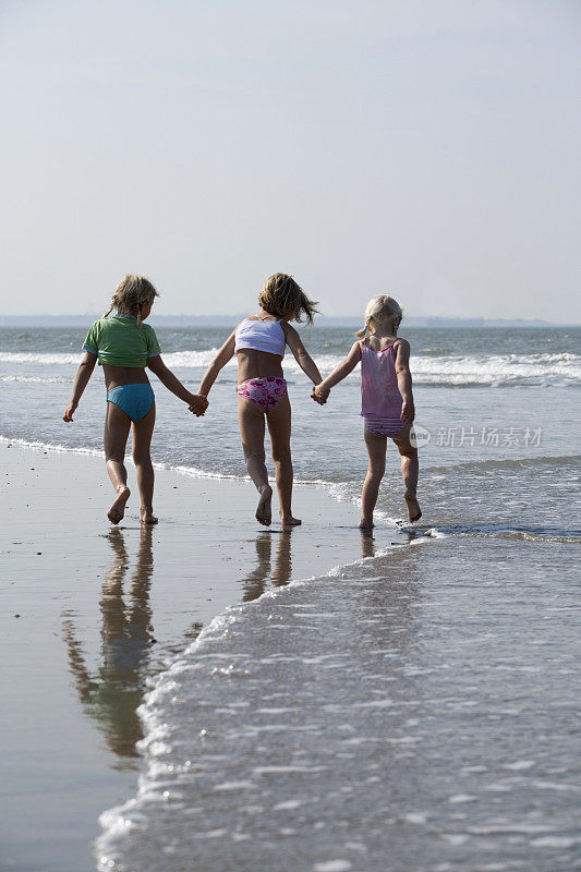 三个小女孩手牵着手沿着海滩散步