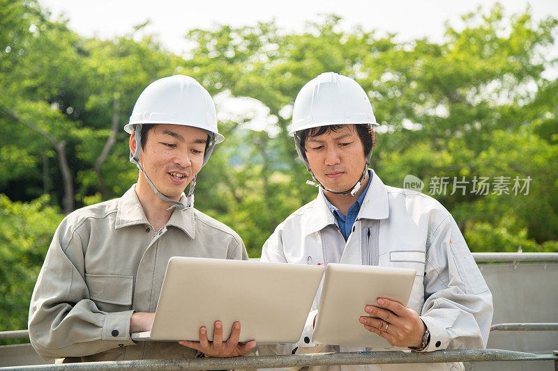 两个建筑工人一边看着数字计算机一边交谈