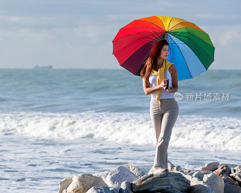 在海边的岩石上，拿着彩色伞的女人