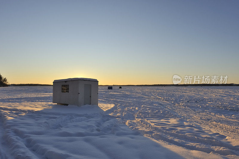 夕阳下冰冻湖面上的鱼冰屋