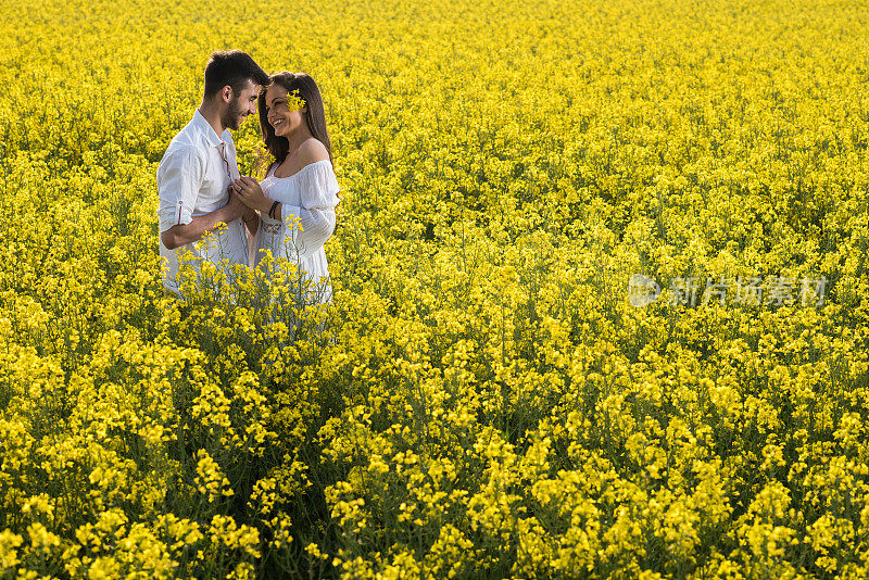一对年轻的情侣站在黄花草地上。