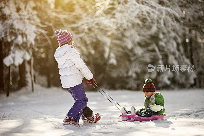 妹妹拉着小弟弟在雪橇上。