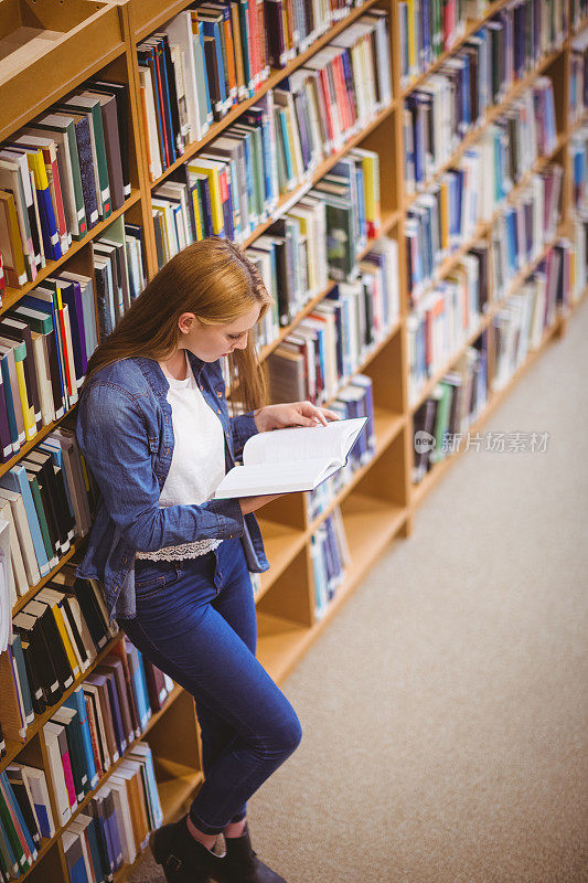 学生倚着书架在图书馆看书