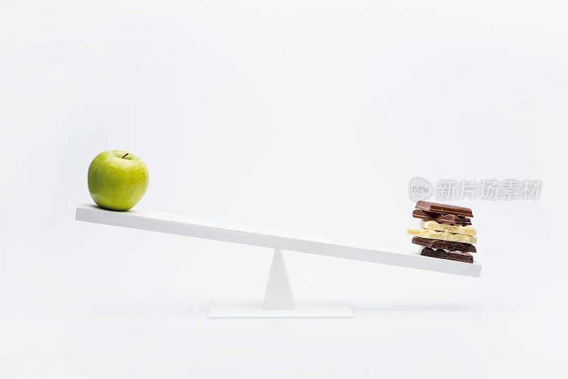 苹果和巧克力在跷跷板上平衡的特写，健康的生活理念
