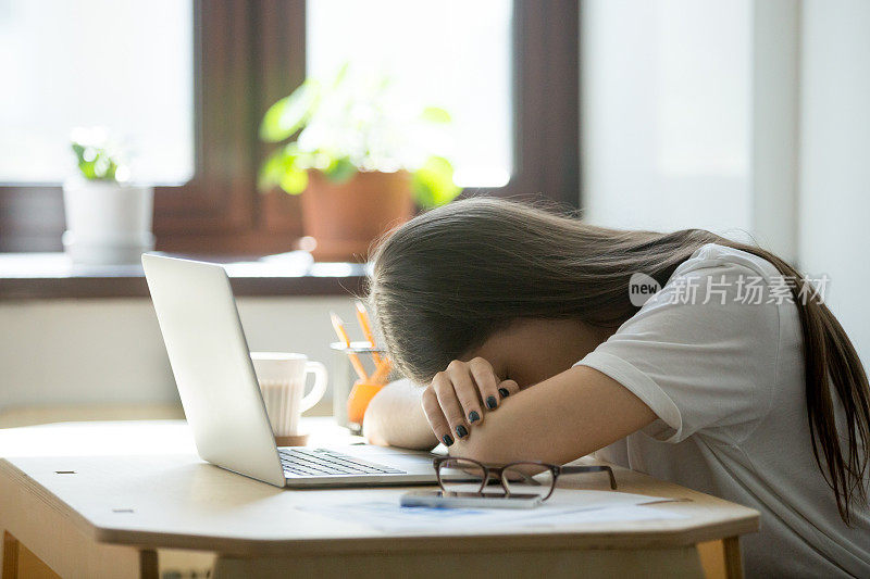 劳累过度，精疲力竭的女商人睡在家庭办公室的笔记本电脑上