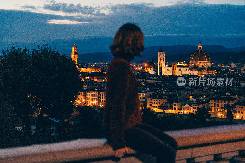 一个女人坐在篱笆上，看着弗洛伦斯的夜景