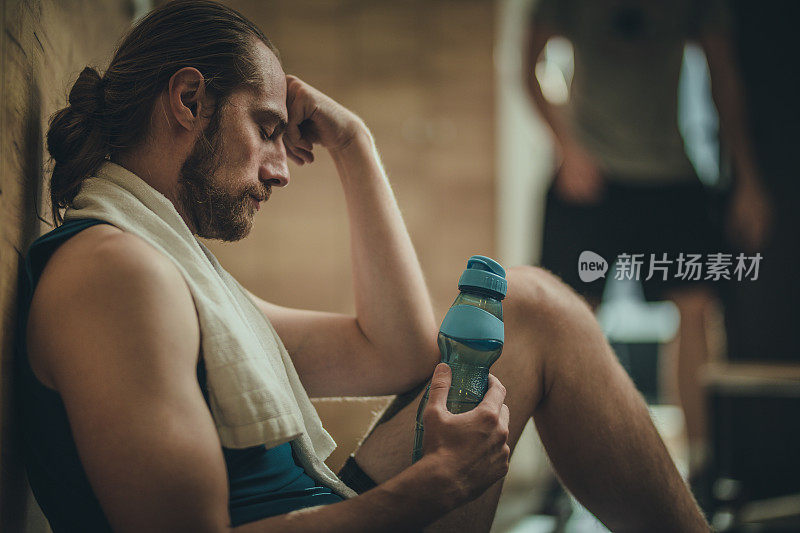 疲惫的运动员在健身房更衣室的水休息。
