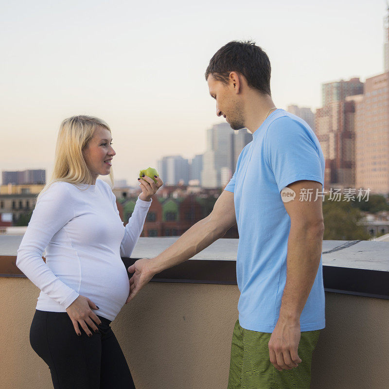 这对年轻的白人夫妇，男人和怀孕的女人，在屋顶上聊天和休息