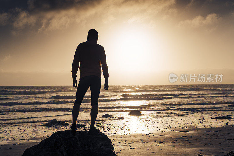 一名男子沿着海滩跑步后，站在日落时分的海滩上。