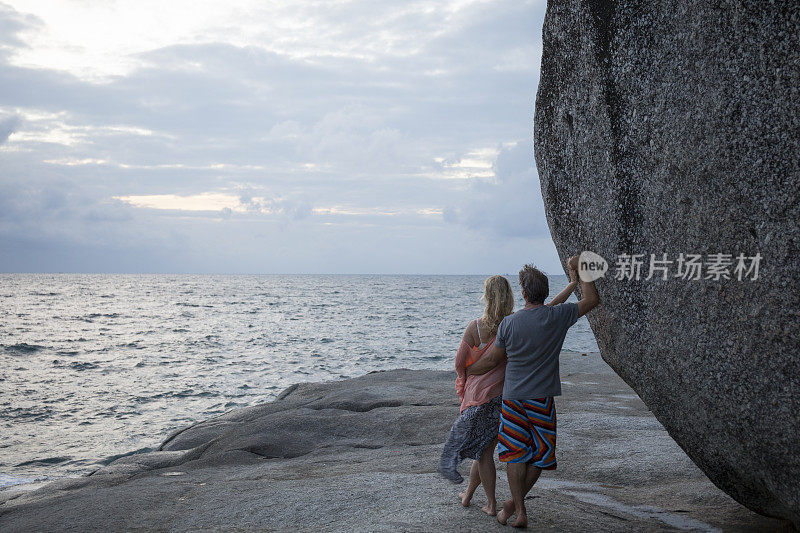 一对夫妇靠在海岸线上的巨石上