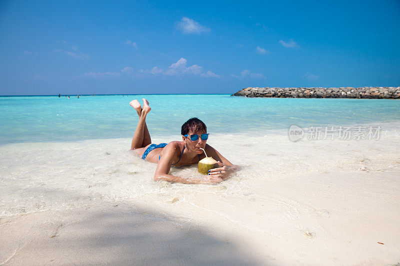 年轻女子在热带海滩上享受椰子汁
