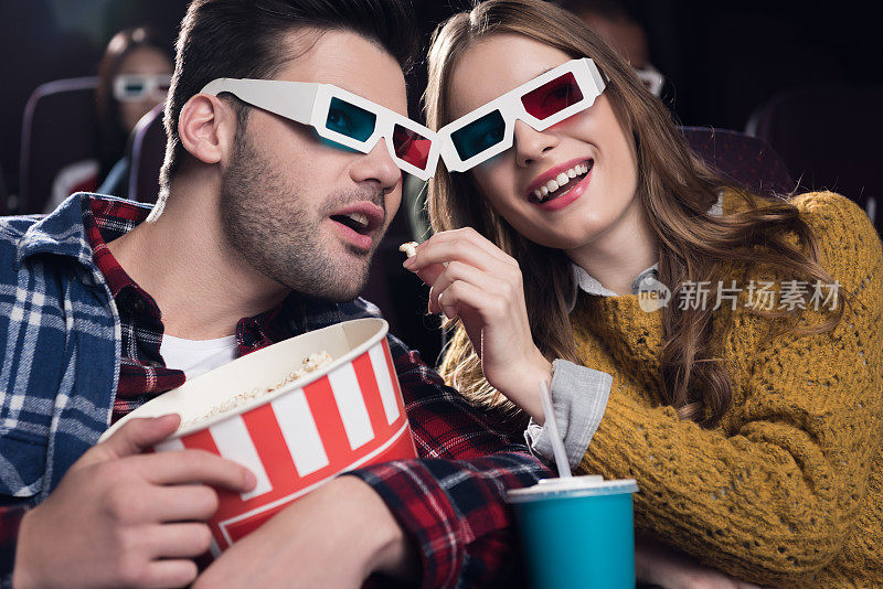 一对戴着3d眼镜的年轻夫妇在电影院边看电影边吃爆米花