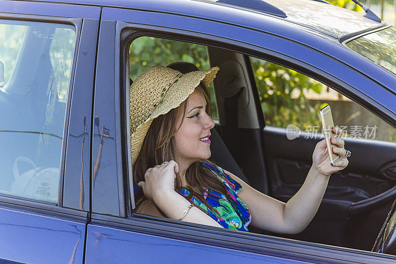 微笑的年轻女子在车内用智能手机自拍
