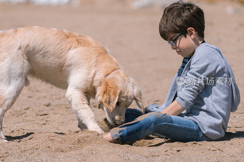 快乐的男孩和她的狗坐在海滩上。