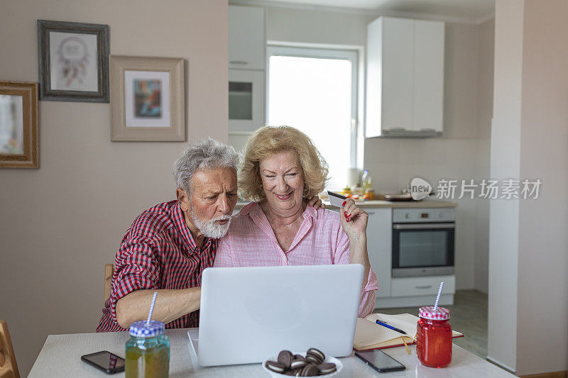 网上购物是最好的购买方式。幸福的老夫妇谈论使用笔记本电脑一起吃早餐，惊讶兴奋的年长妇女看着电脑屏幕上显示微笑的中年丈夫在网上购物在网站上销售