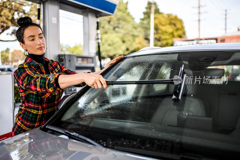 一个时髦时髦的女人在加油站擦拭挡风玻璃