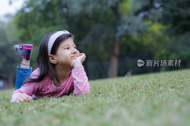 可爱的小女孩迈着可爱的笑容躺在公园的草地上