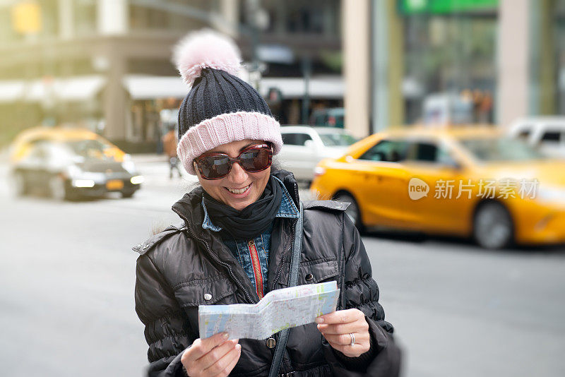 SoloTravellers。一名女游客在冬天参观纽约，微笑着看城市地图