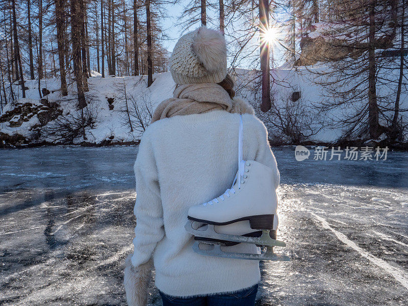 一个年轻女子肩上扛着冰鞋走在结冰的湖面上