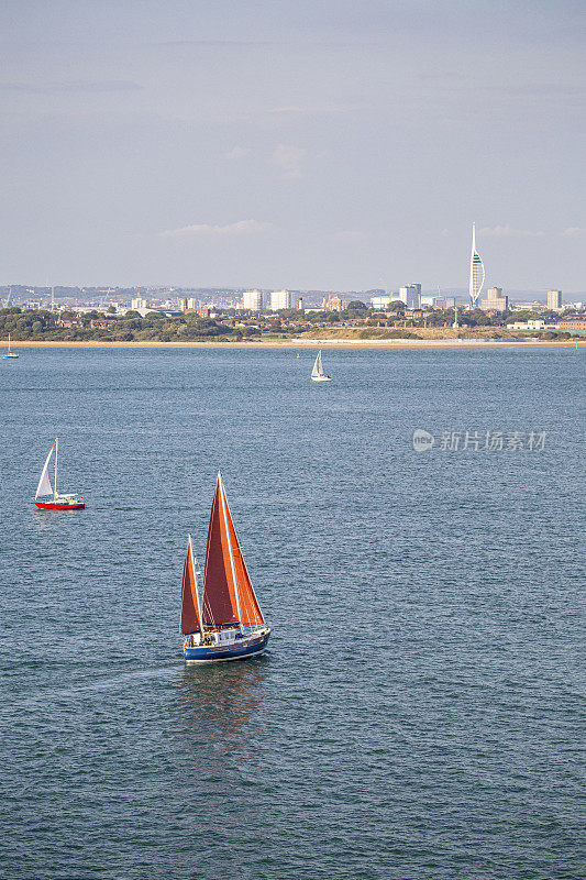 从一艘游轮的甲板上拍摄的阿联酋三角帆塔和朴茨茅斯港的远景，前景中有几艘帆船。