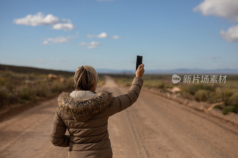 一位女性正在乡间的砾石路上寻找手机信号。