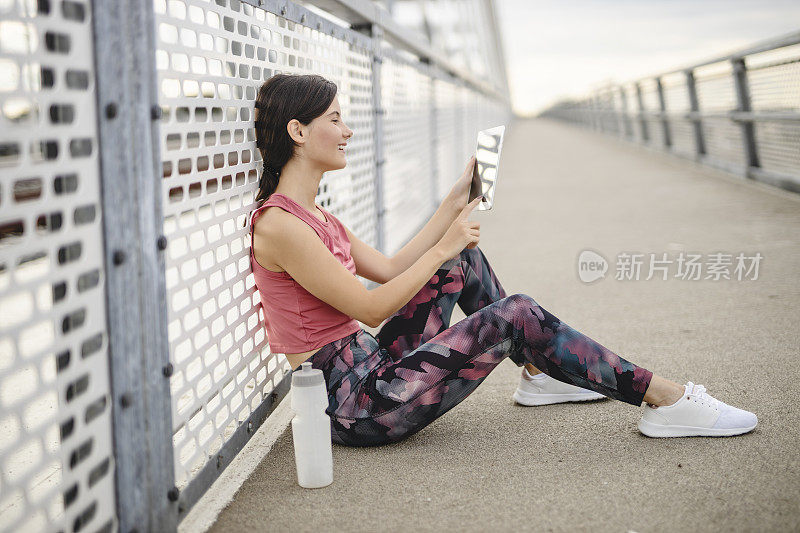 运动迷人的年轻女子使用数码平板电脑，喝水和休息后，户外慢跑