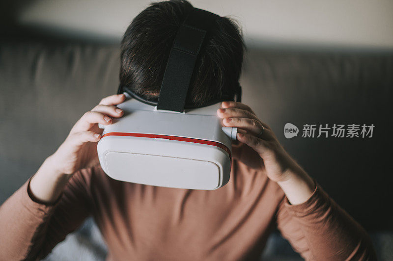 一个亚裔中国中年女性在客厅里使用VR谷歌玩VR虚拟现实在线游戏