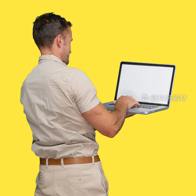 白人男性体力劳动者站在黄色背景穿着纽扣衬衫，拿着盒子和使用电脑
