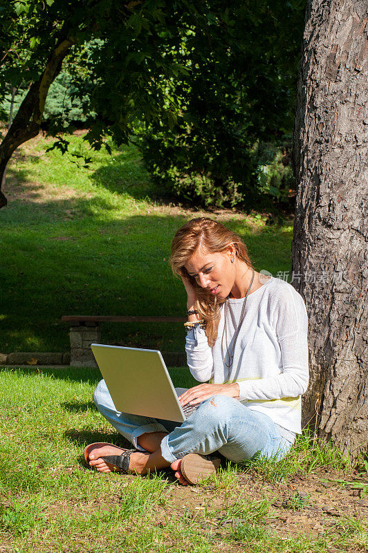 漂亮的女人一边工作一边用笔记本电脑打字一边坐在公园里