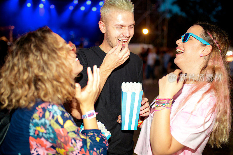 三个朋友在晚上的现场音乐节上吃着爆米花大笑