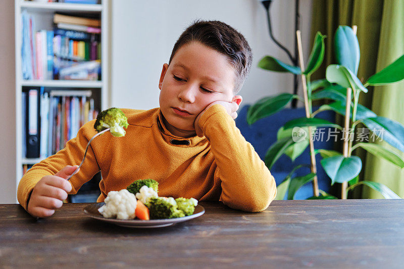 孩子对不得不吃蔬菜很不高兴。他的盘子里有许多蔬菜。他讨厌蔬菜。