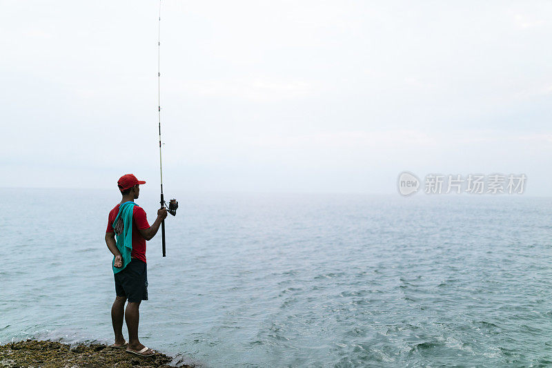 亚洲男子戴着帽子在海滩上钓鱼