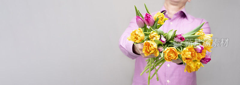 一个白种人，送了一束明媚的春天的花，一束郁金香。一大束黄色和紫色的郁金香。