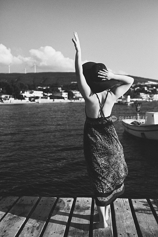 美丽的女人穿着衣服和帽子在码头上看海，背影，黑白照片